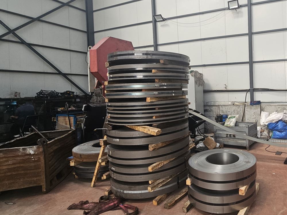 Steel coils stacked on the shop floor next to a decoiler