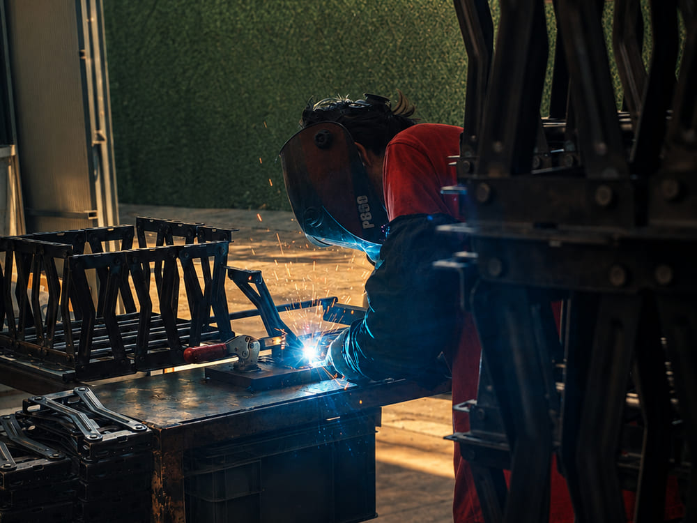 Operator in a welding mask welding a scissor arm at the bench